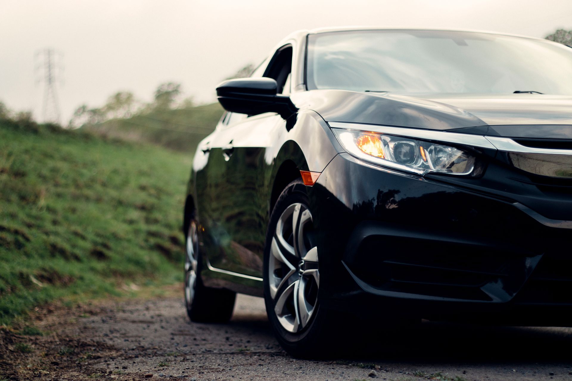 Black car parked on a dirt road, next to grassy hill, daytime.