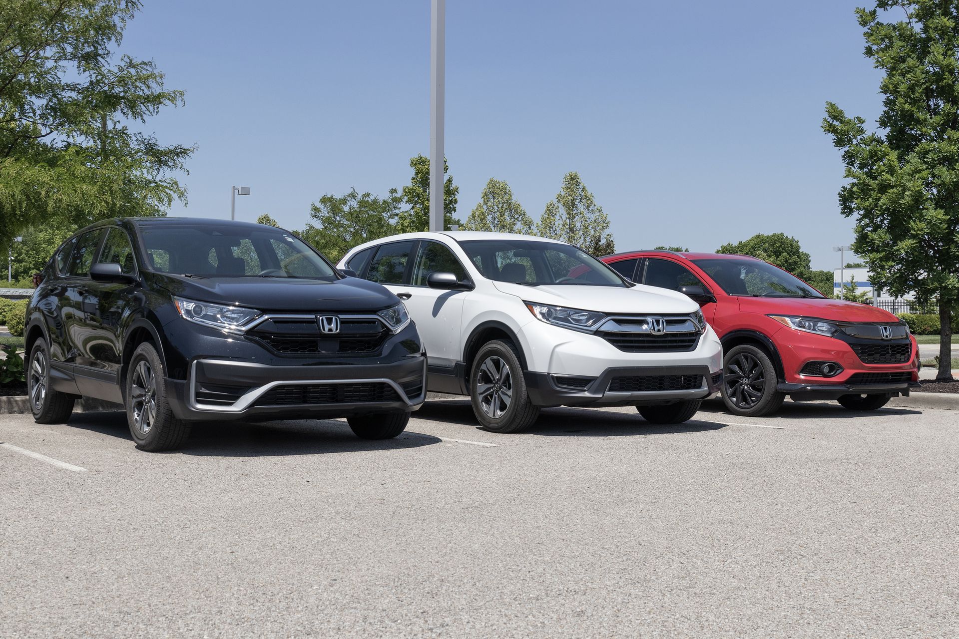 Three SUVs parked outdoors, black, white, and red, under a bright sky.