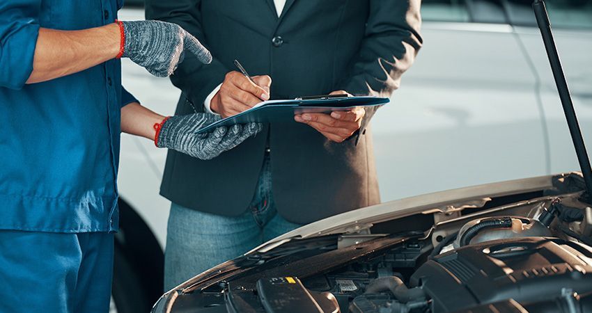 a man in a suit is standing next to a mechanic looking at a clipboard .
