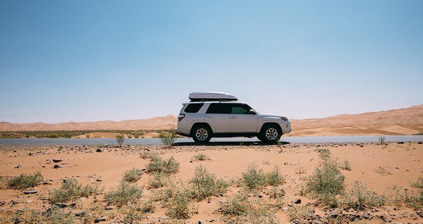 a white suv with a roof rack is driving down a desert road .