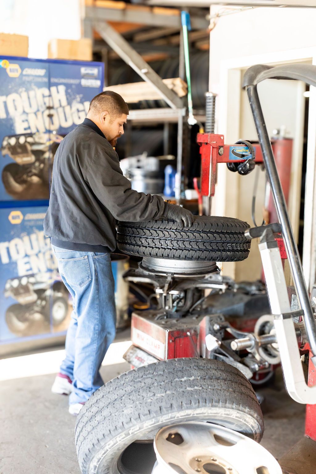 A man is working on a tire in front of a sign that says tough enough
