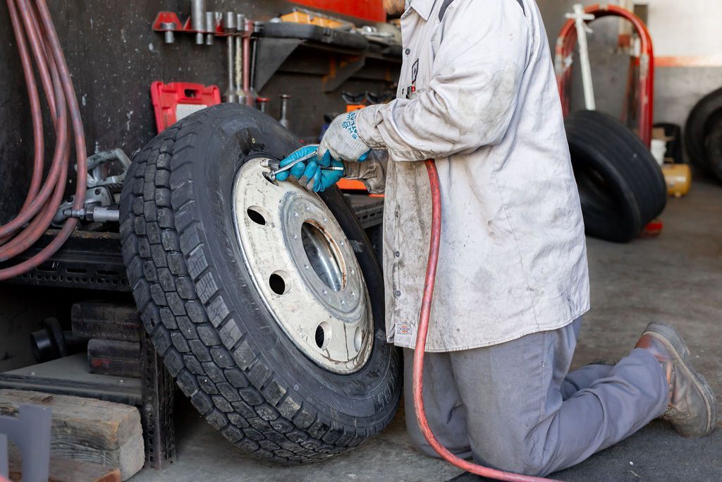A man is kneeling down to change a tire on a truck