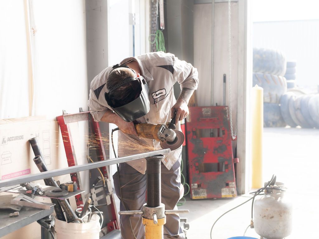 A man wearing a welding mask is grinding a piece of metal