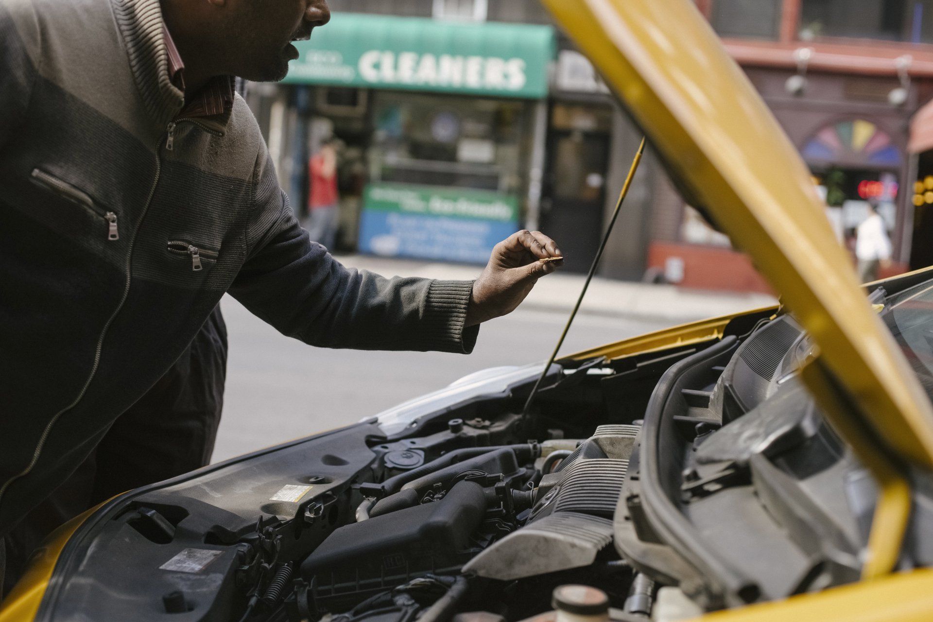 A man is looking under the hood of a yellow car