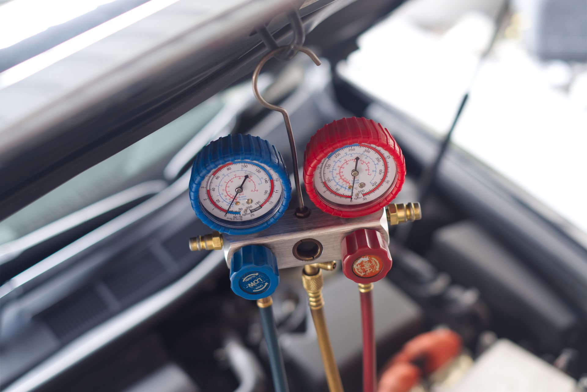 Blue and red manifold gauges hanging inside a car engine bay