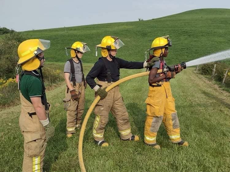 Firefighters training with a hose in a grassy field.