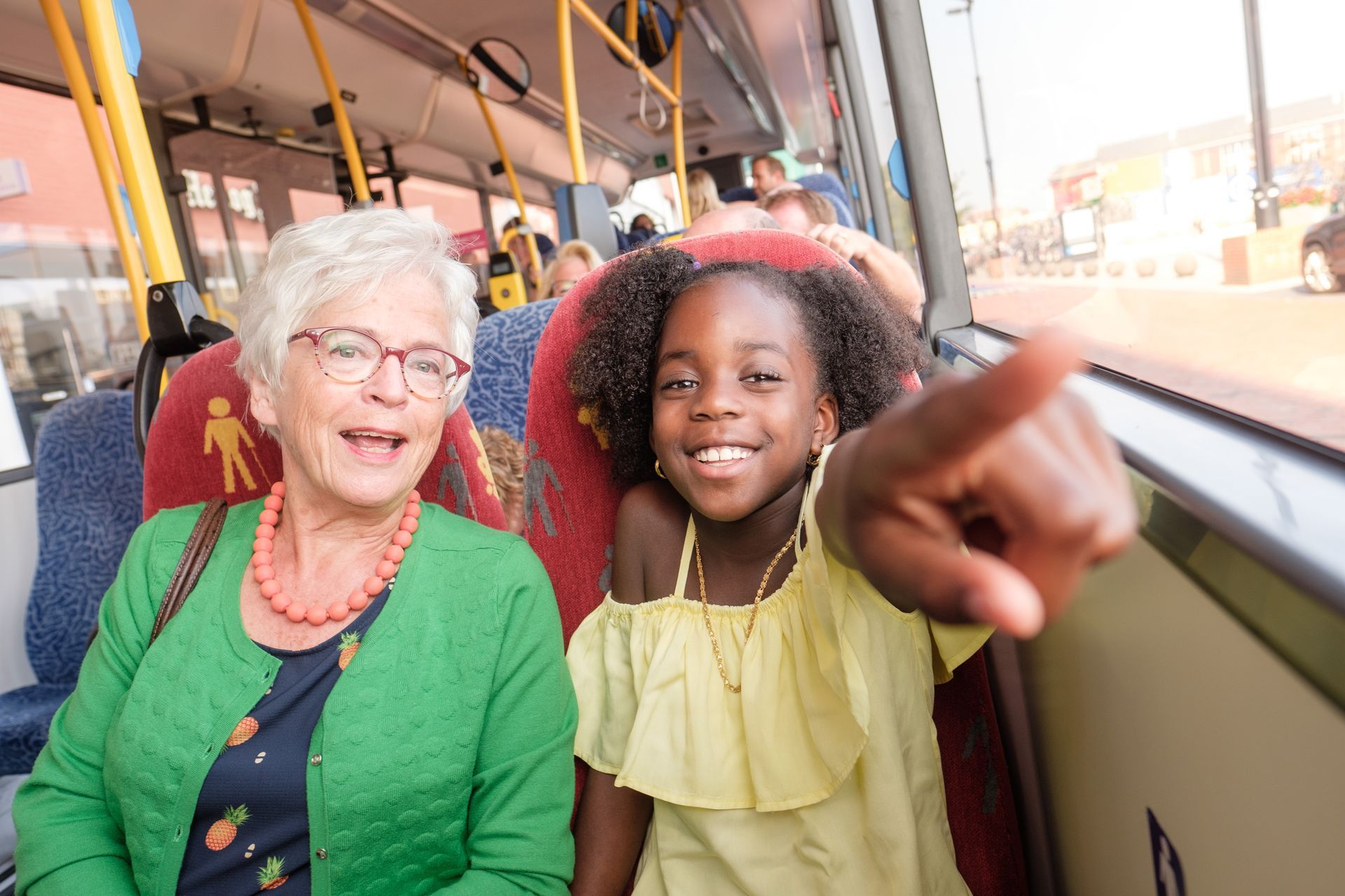 Oma en kleindochter gezellig op stap met de bus. Kleindochter wijst aan wat ze ziet.