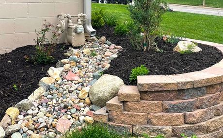 A stone wall is surrounded by rocks and mulch in a garden.