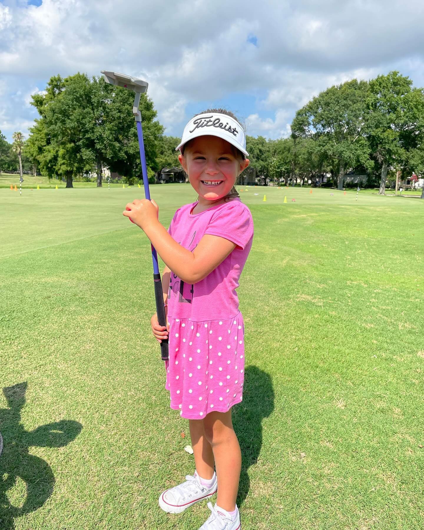 A little girl is holding a golf club on a golf course.