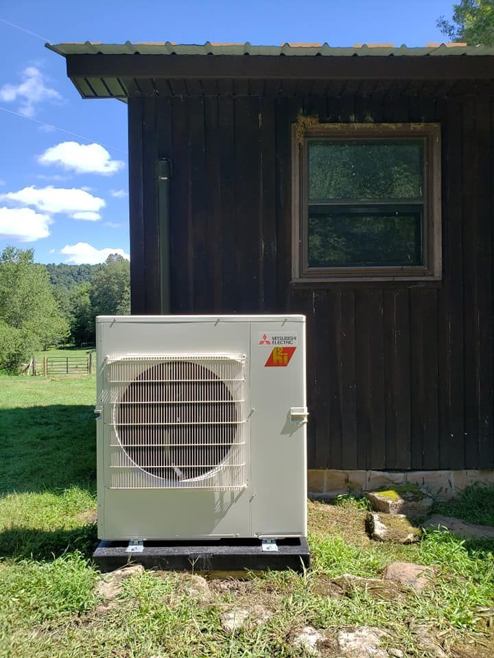 A white air conditioner is sitting in front of a wooden building.