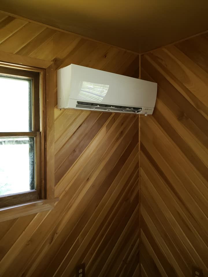 A white air conditioner is mounted on a wooden wall next to a window.