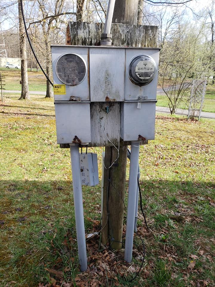 An old electrical box is sitting on top of a wooden post in the grass.