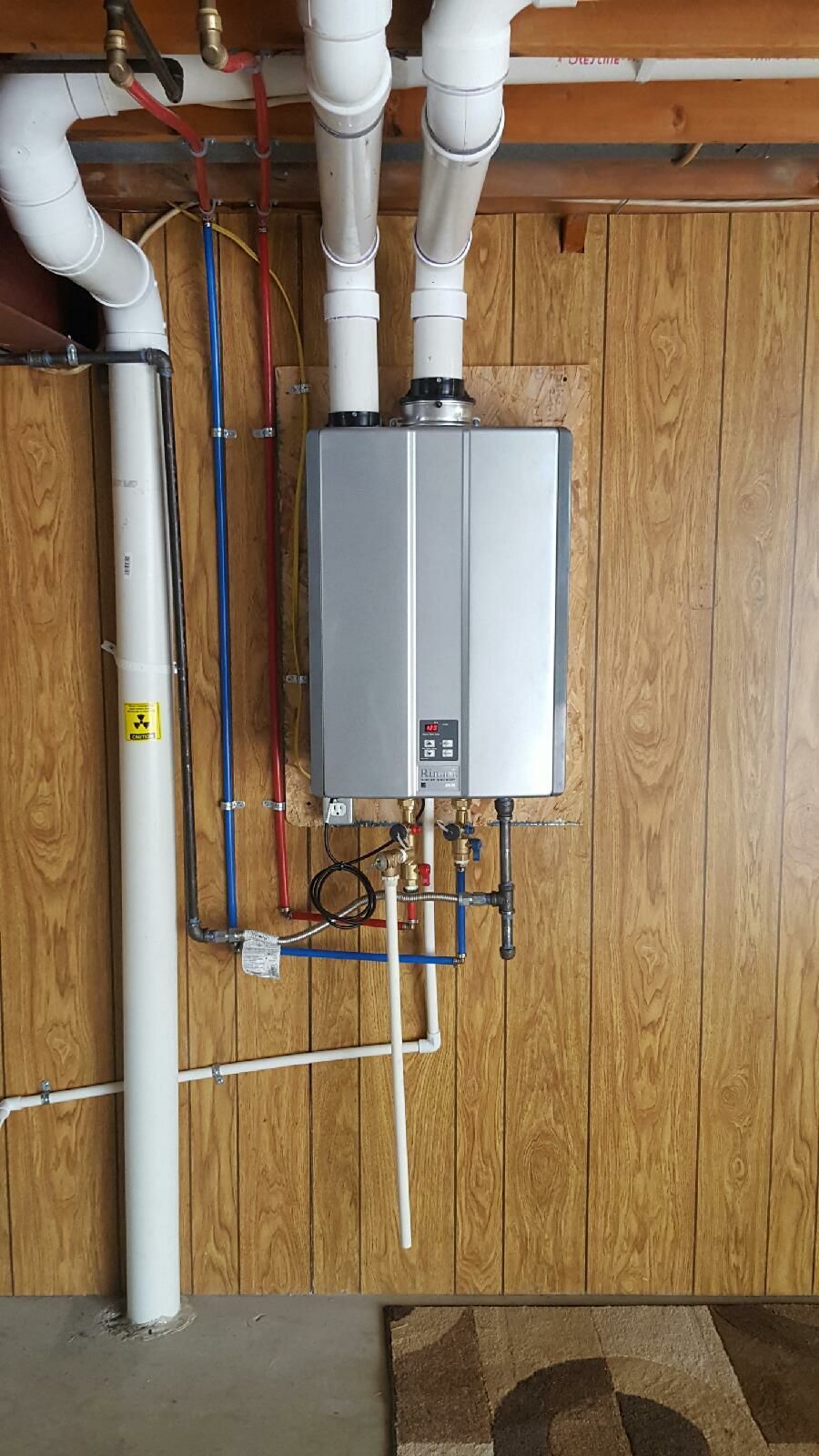 A water heater is hanging on a wooden wall in a basement.