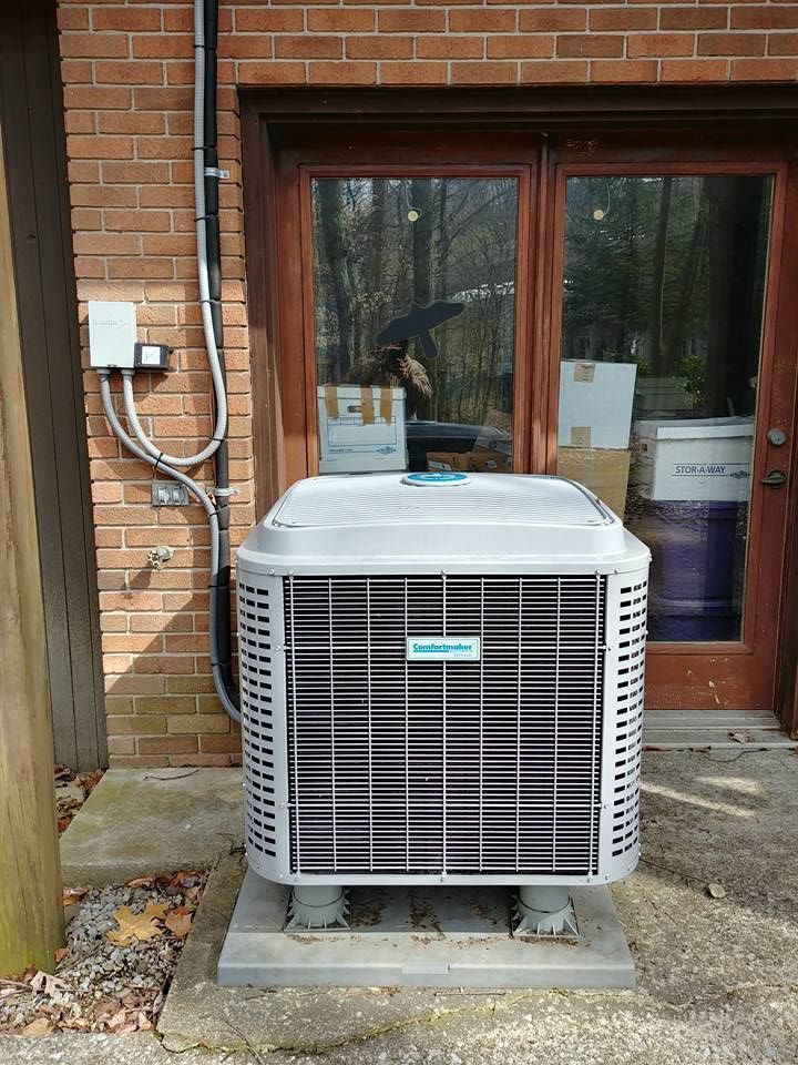 A large air conditioner is sitting outside of a brick building.