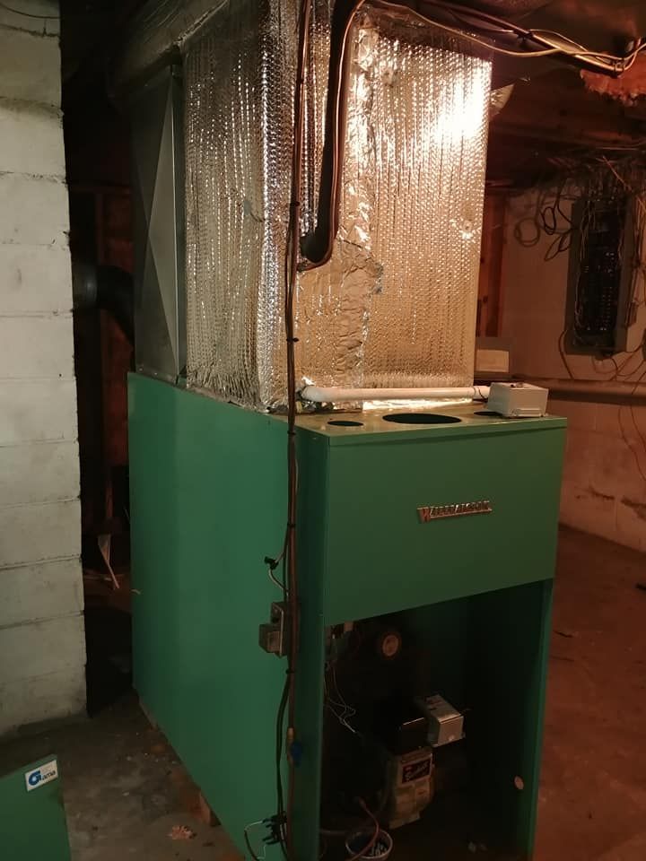 A green boiler is sitting in a basement next to a wall.