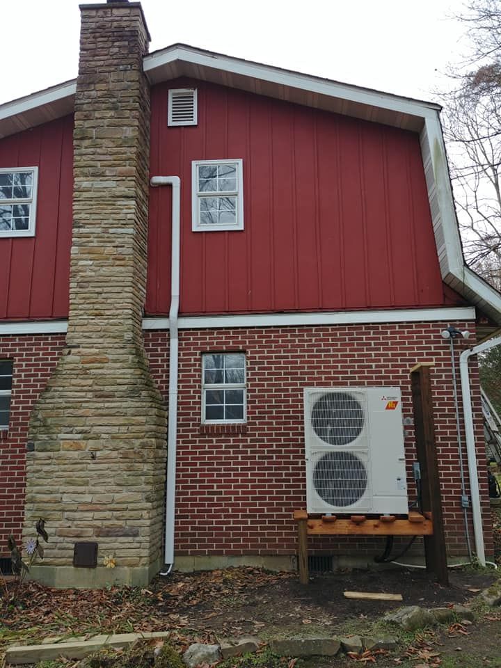 A red brick house with a chimney and a white air conditioner on the side.