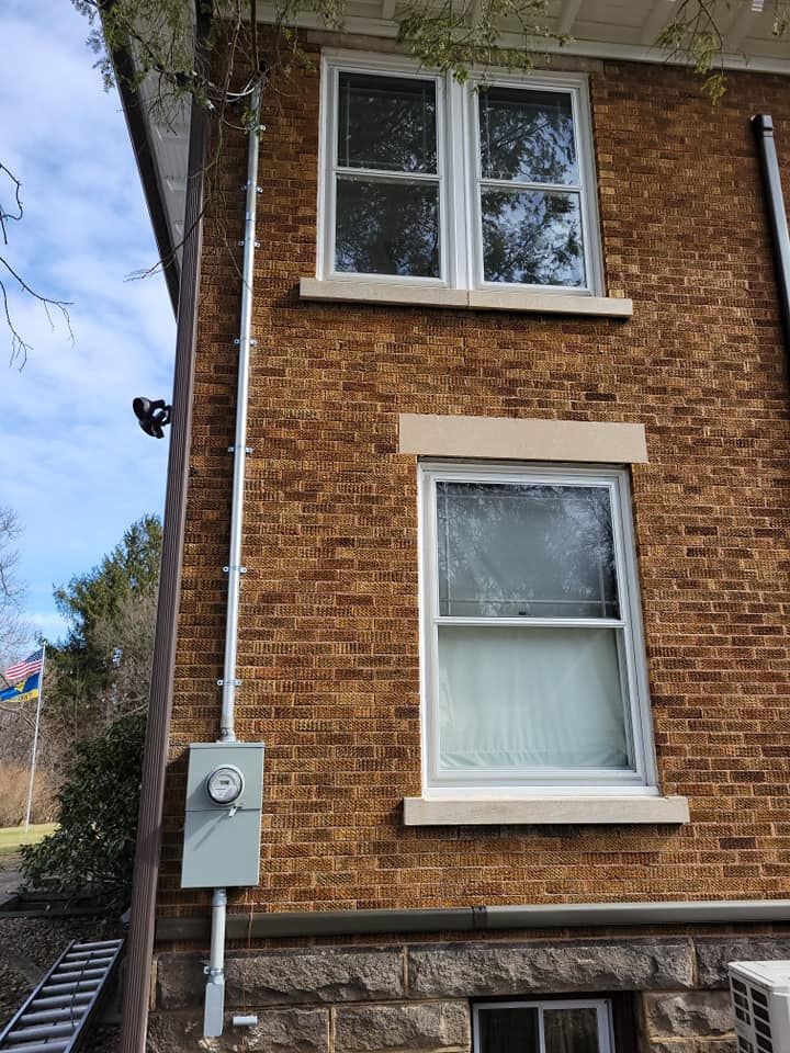 A brick building with two windows and a ladder in front of it.