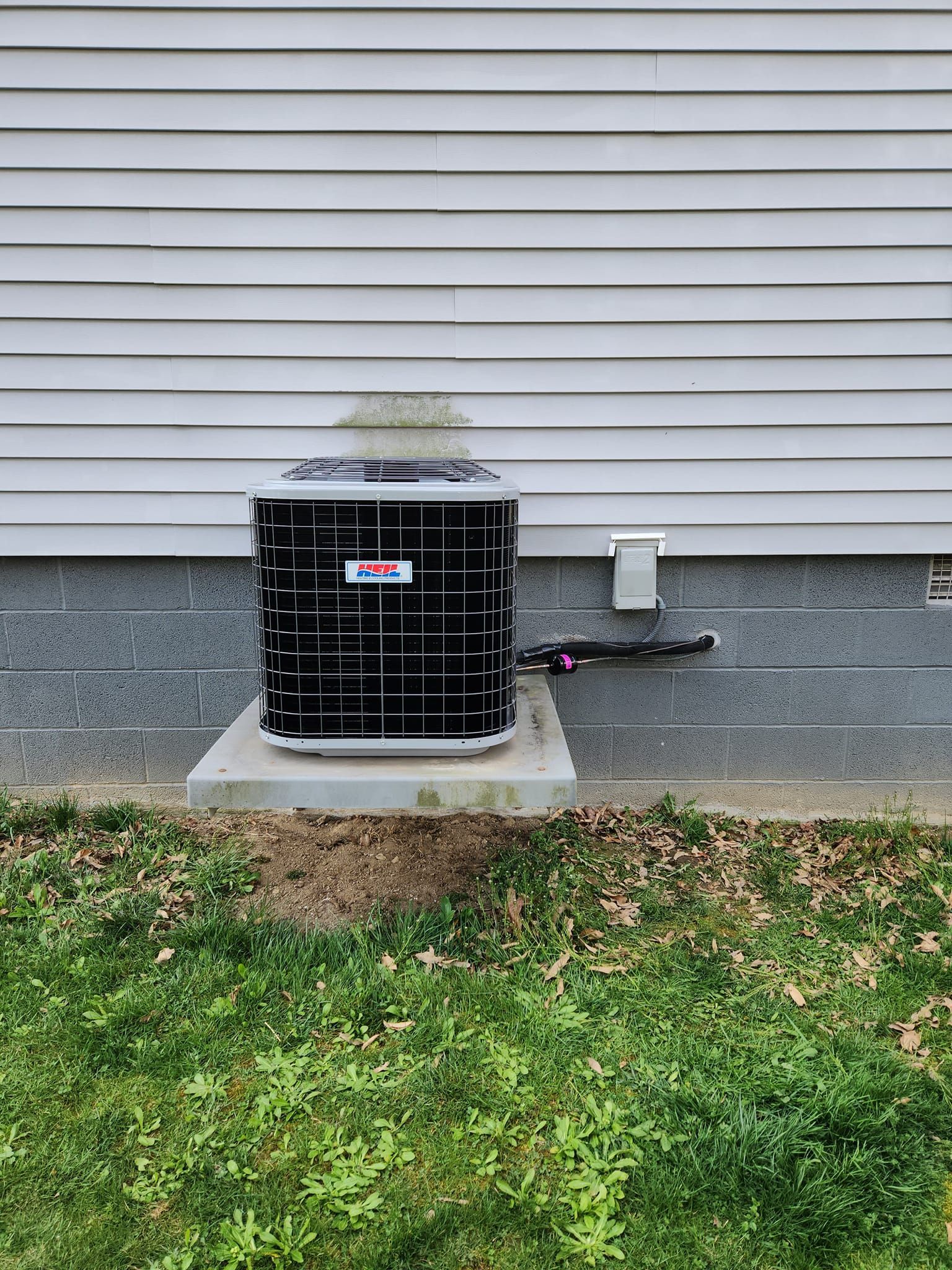 A black air conditioner is sitting on the side of a house.