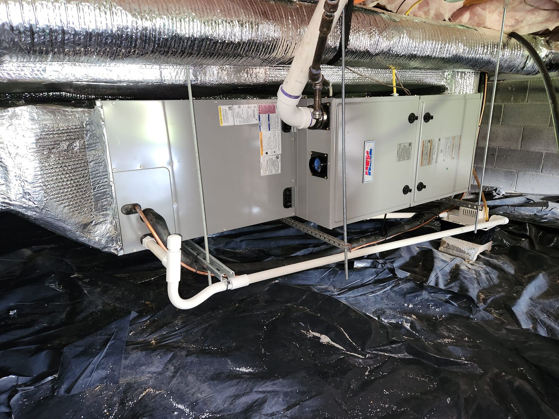 An air conditioner is sitting underneath a ceiling in a basement.