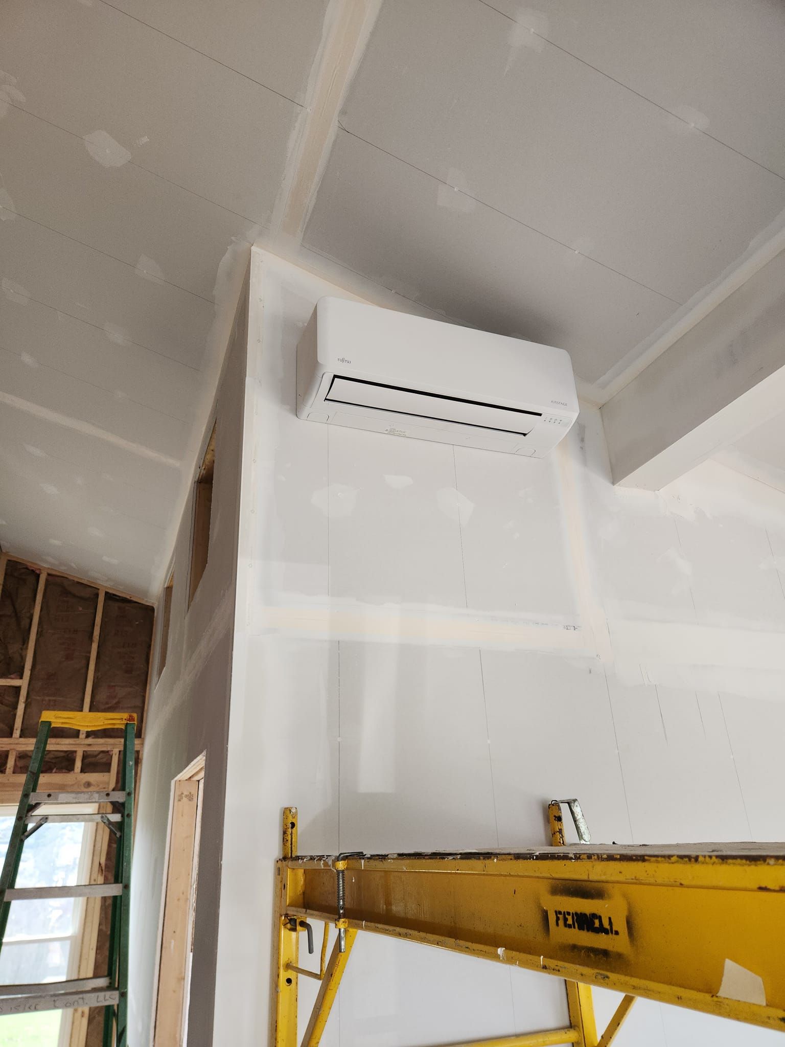 A white air conditioner is hanging from the ceiling of a room under construction.
