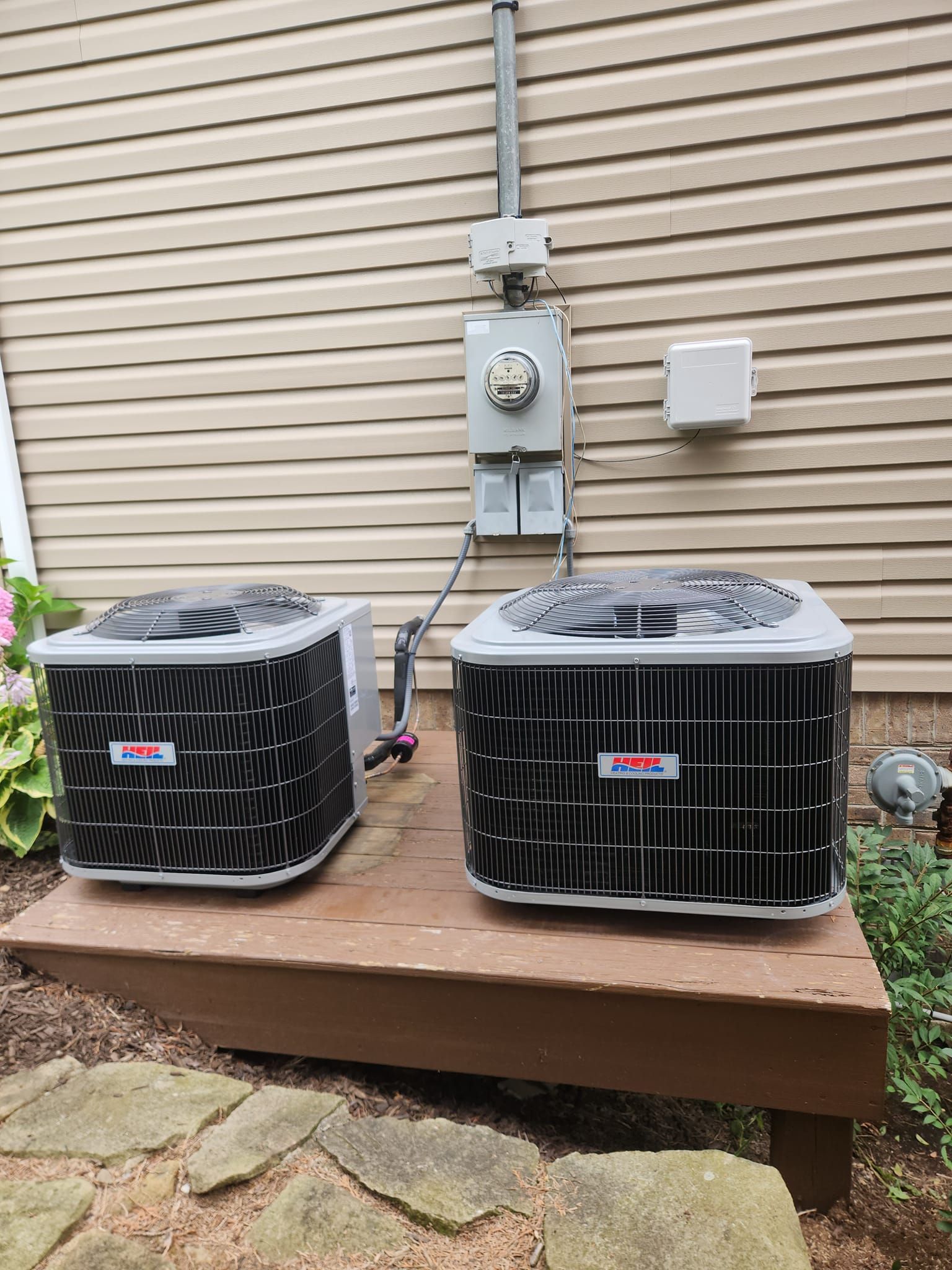 Two air conditioners are sitting on a wooden deck in front of a house.
