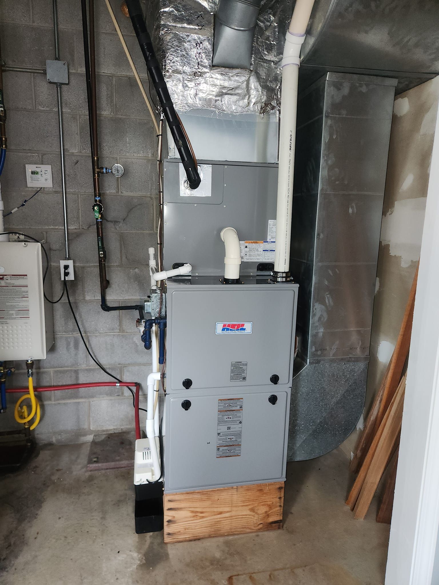 A gas heater is sitting in a basement next to a brick wall.