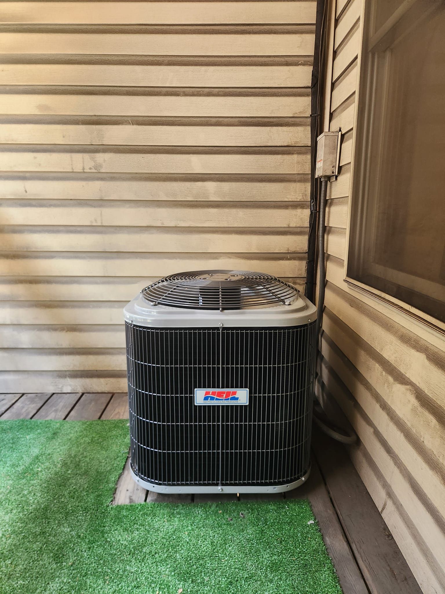 An air conditioner is sitting on the side of a house next to a window.