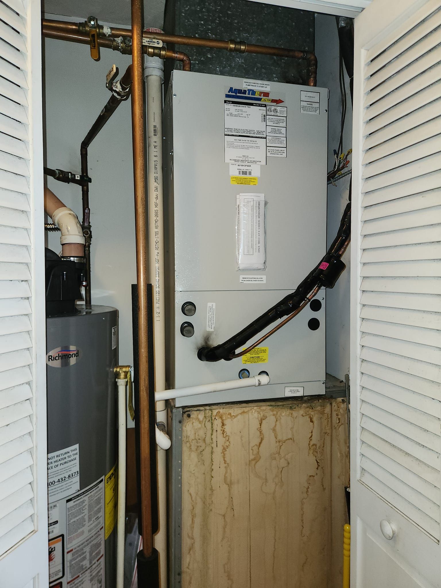 An air conditioner is sitting on top of a wooden box in a closet.