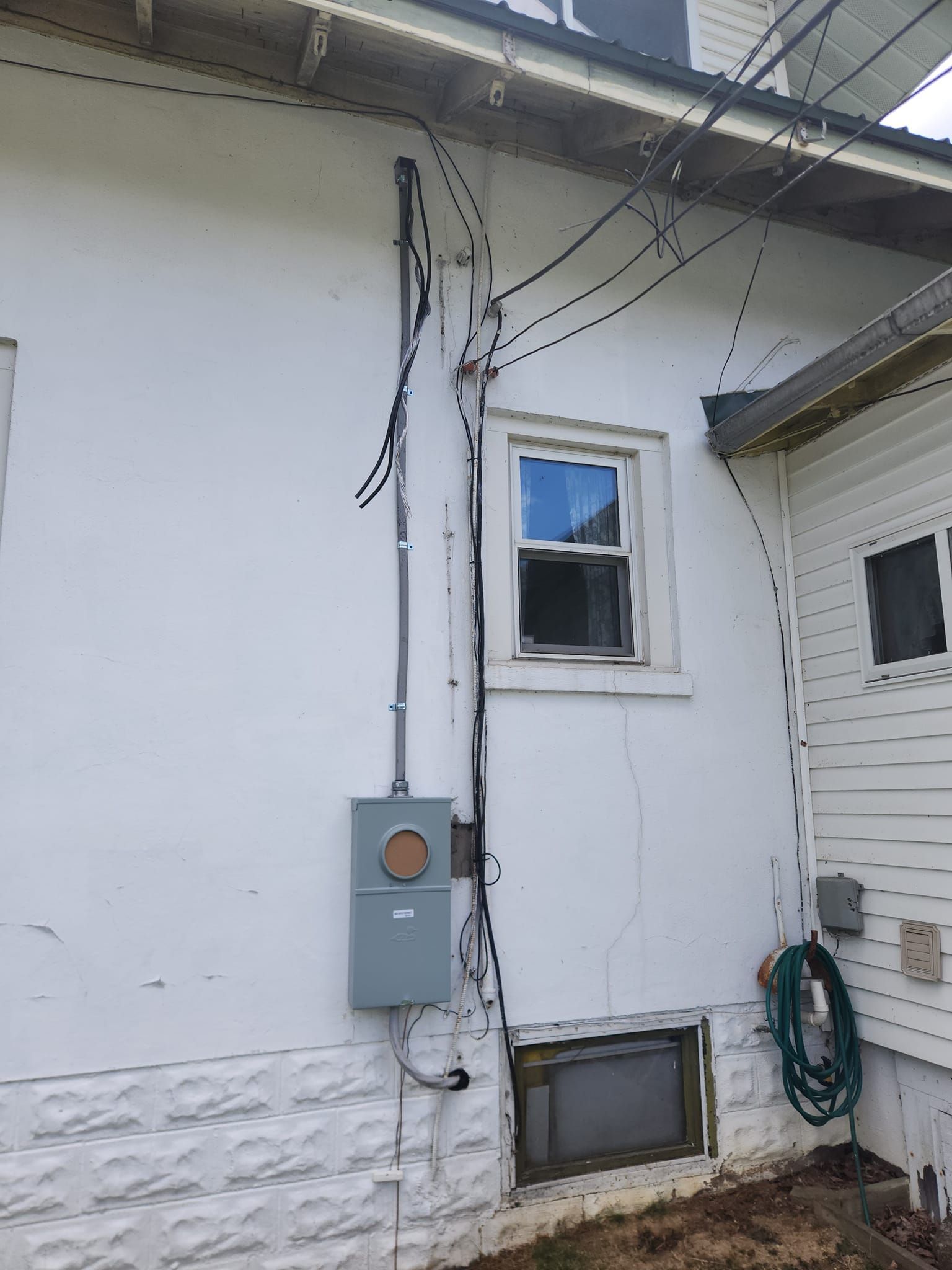 A white house with a window and a hose on the side of it.