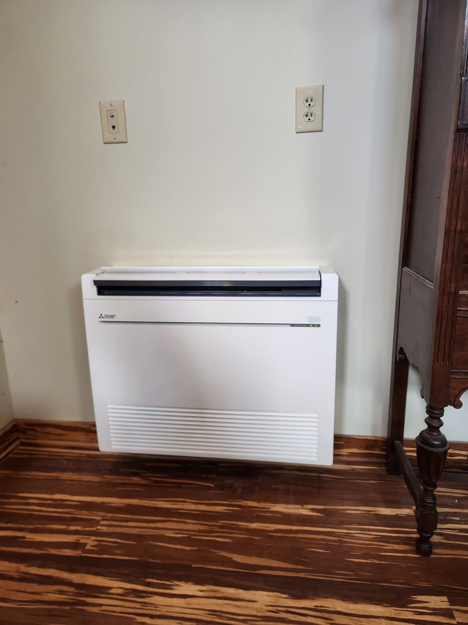 A white air conditioner is sitting on a wooden floor in a room.