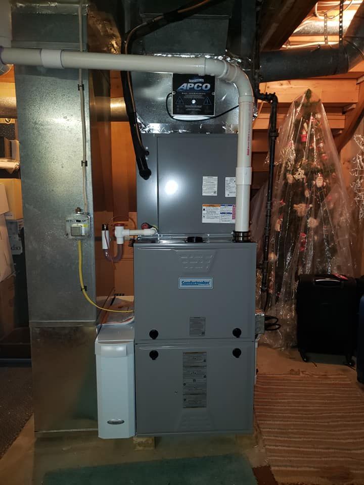 A furnace is sitting in a basement next to a christmas tree.