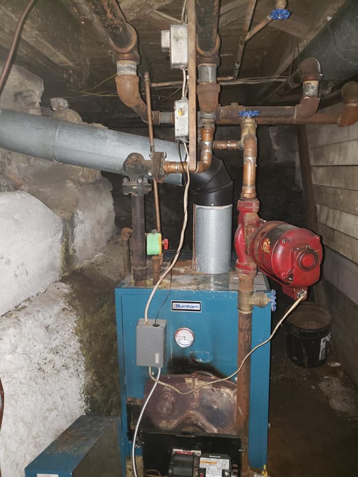 A blue boiler is sitting in a basement surrounded by pipes