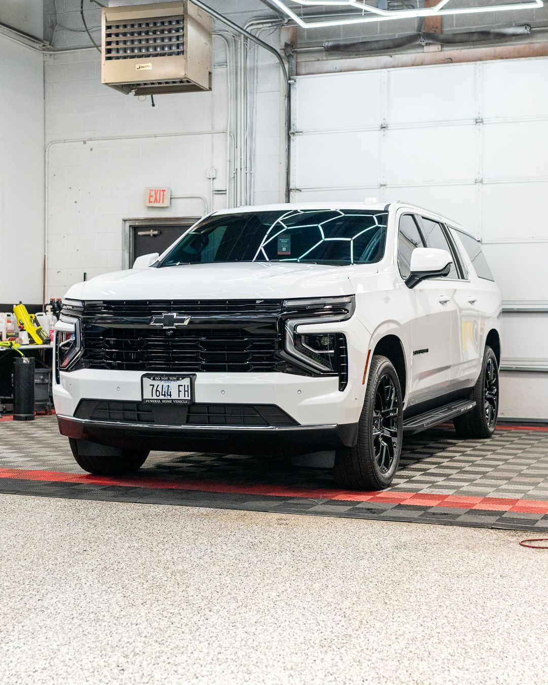 White SUV parked indoors in a garage, facing forward on a patterned floor.