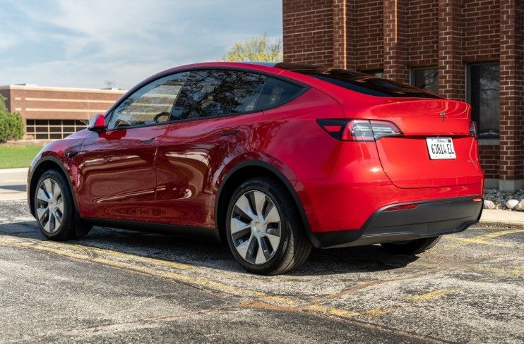 Red Tesla Model Y parked beside a brick building on a sunny day