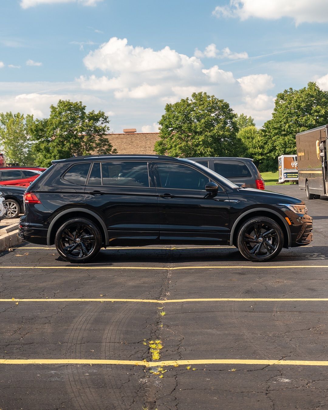 Black SUV parked in a lot under a partly cloudy sky, with other vehicles nearby.