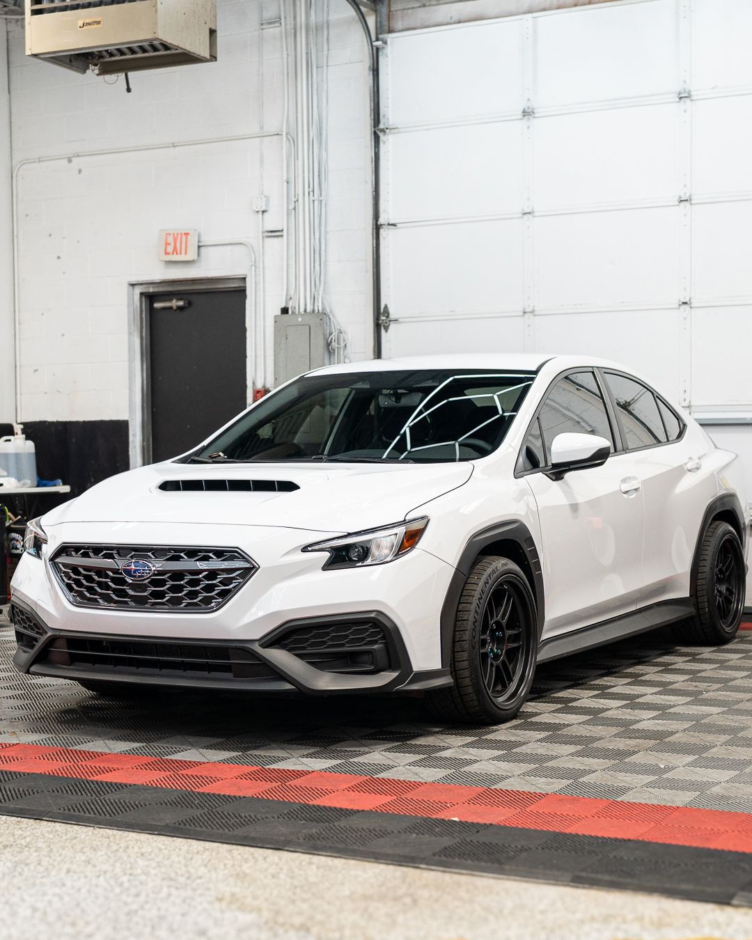 White sporty sedan with black wheels parked indoors in a garage-like showroom