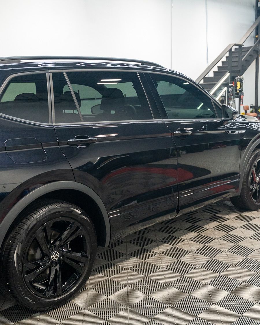 Black SUV parked indoors on a checkered floor, side view with a staircase in the background
