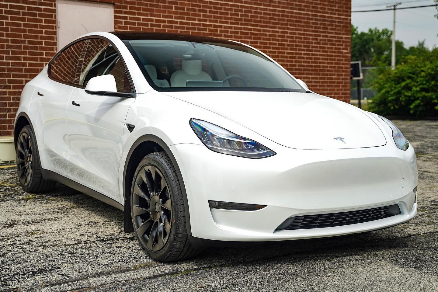 White Tesla Model Y parked in front of a brick building.