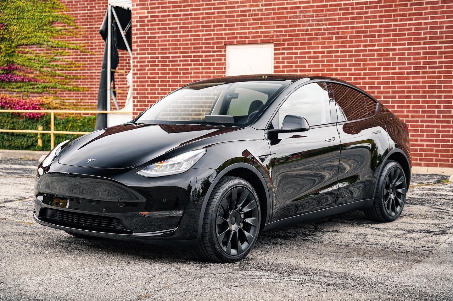 Black Tesla Model Y SUV parked in front of a brick building.