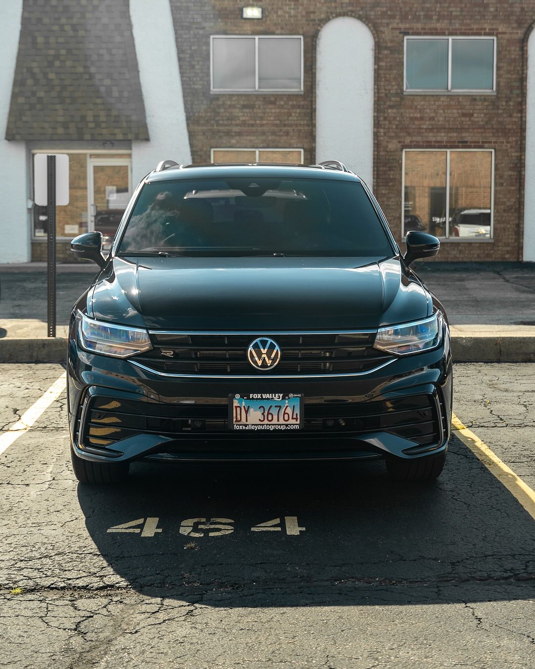 Black Volkswagen SUV parked in a lot in front of a brick building and storefronts.