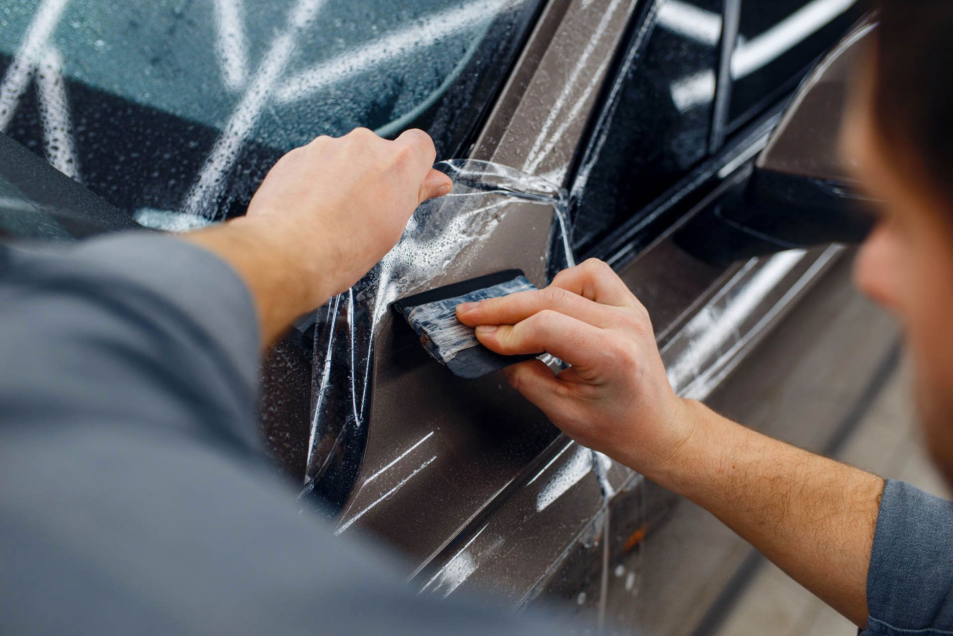Hands applying protective film to a dark car door handle with a squeegee