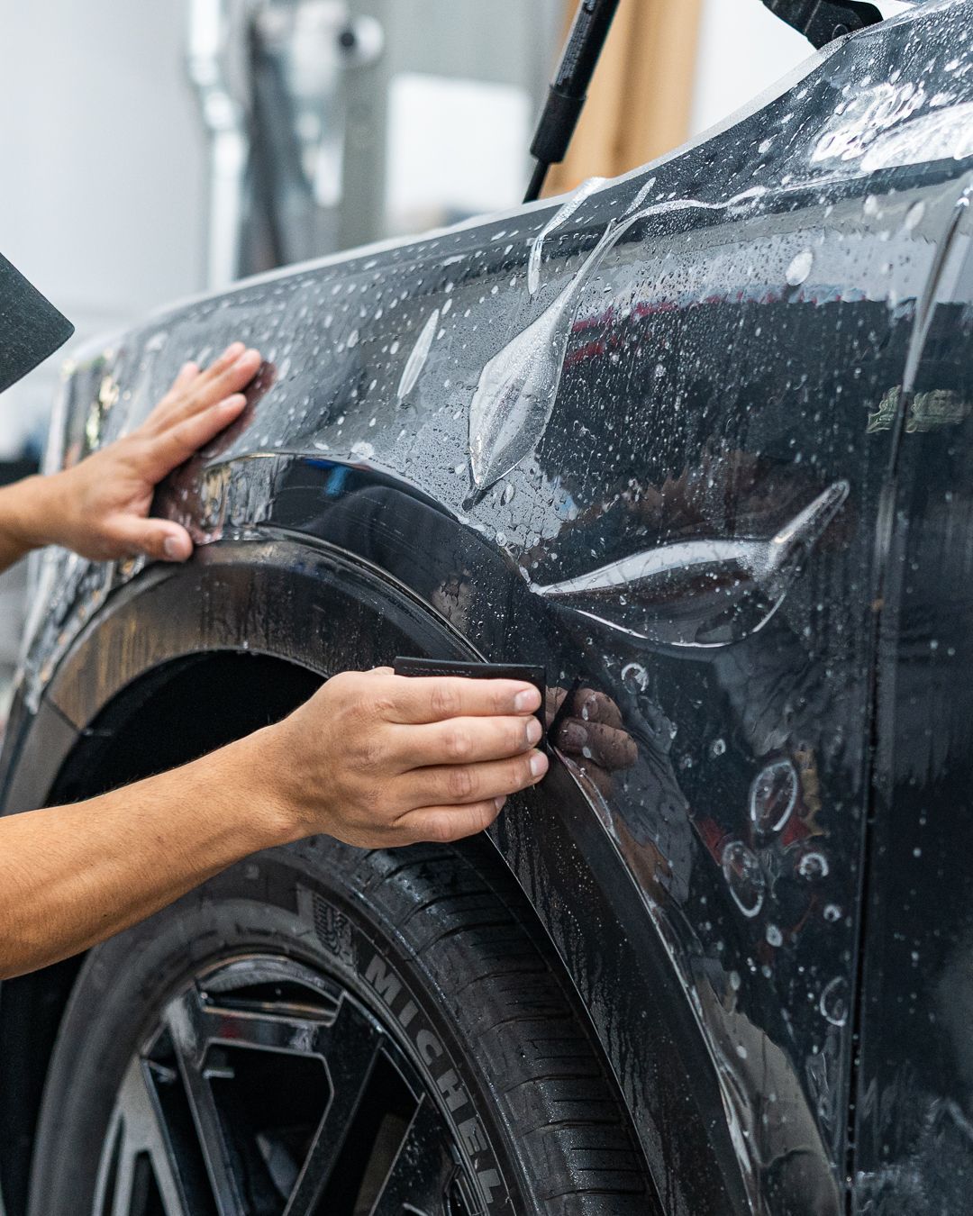 Person applying protective film to a black car's fender, near the tire.