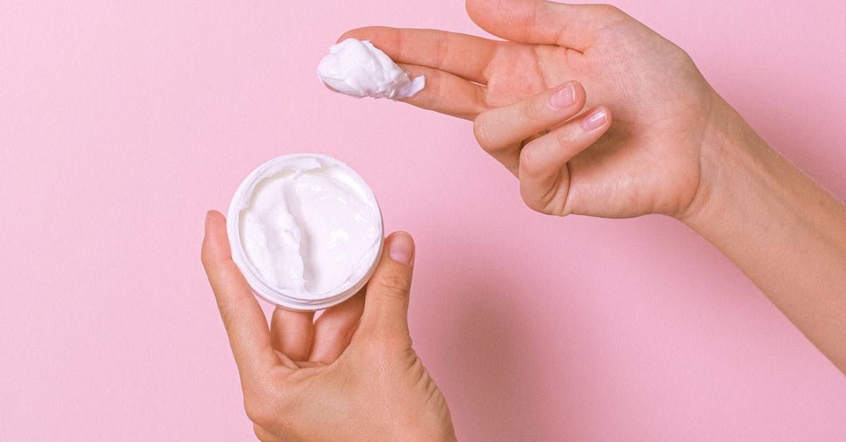 A woman is holding a jar of cream in her hands on a pink background.