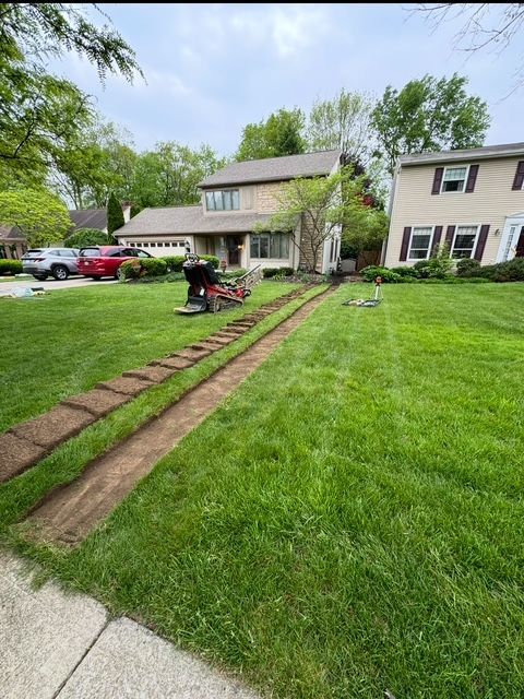 A man is cutting a lawn with a lawn mower in front of a house.