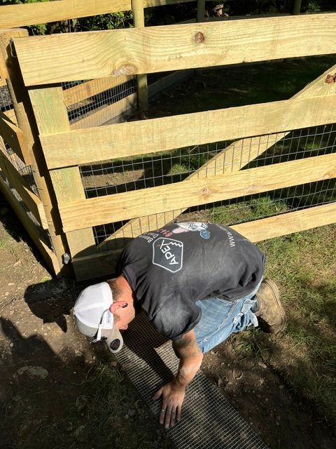 A man is kneeling down in front of a wooden fence.
