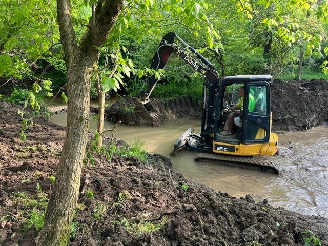 A man is driving a small excavator through a muddy area.