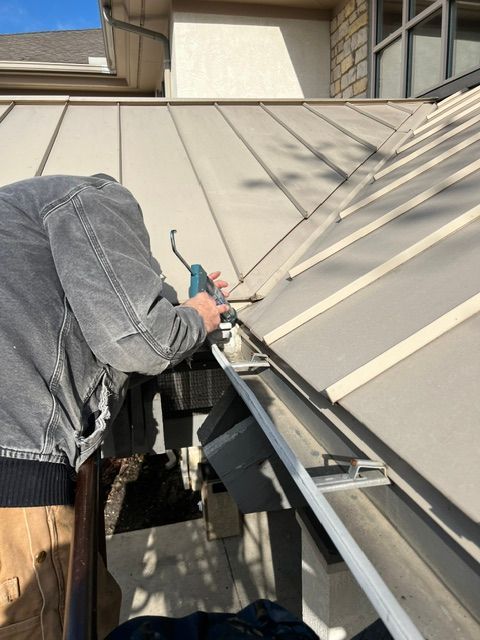 A man is working on a gutter on the roof of a house.