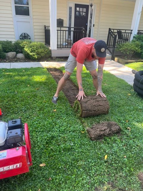 A man is rolling a roll of turf in front of a house.