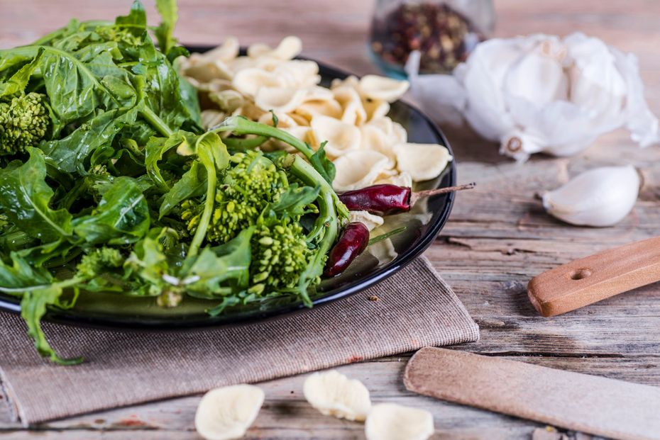 Cime di rapa, pasta, aglio e spezie su un rustico tavolo di legno.