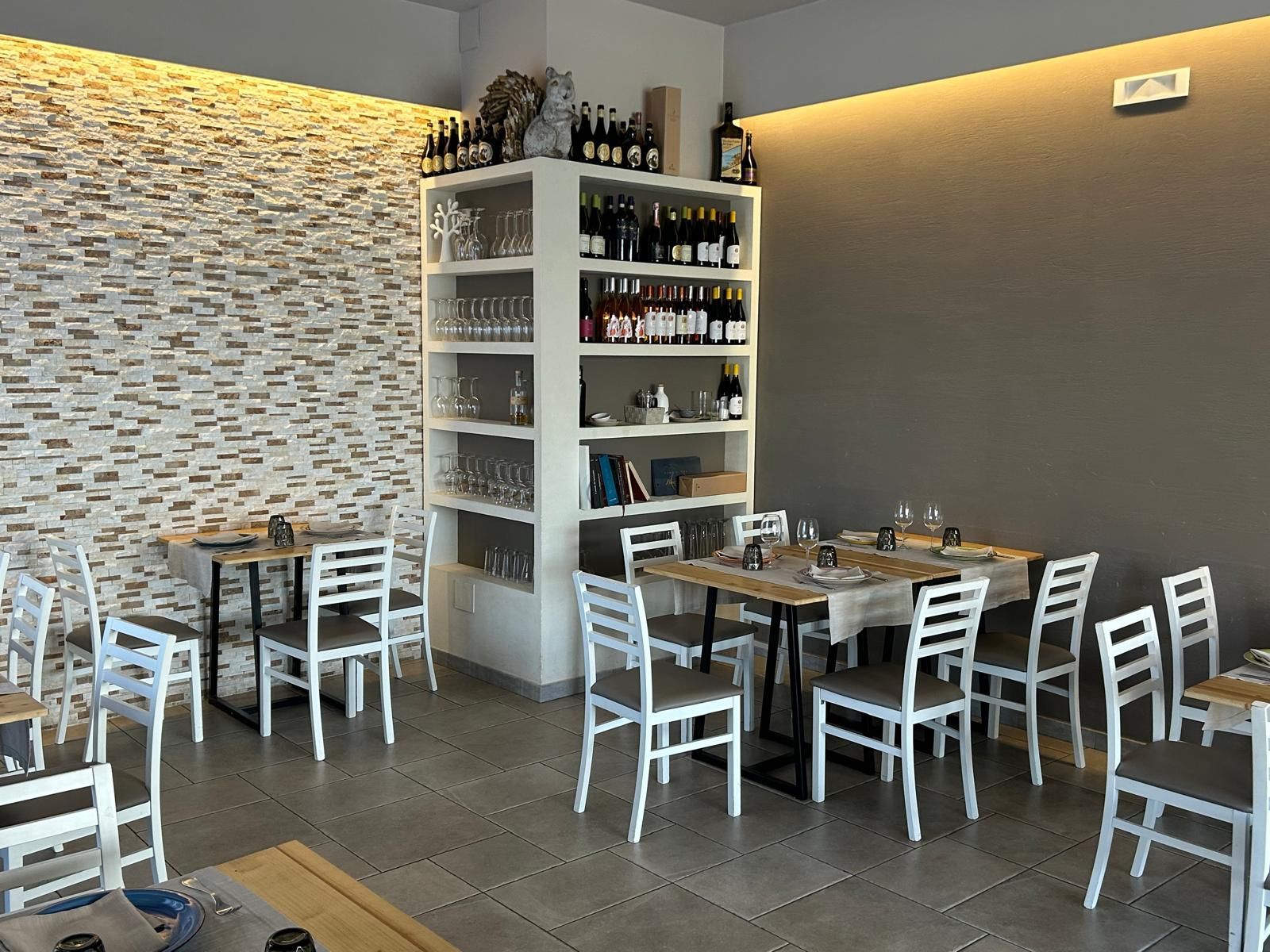 Interno del ristorante con tavoli, sedie e cantina per il vino integrata. I tavoli sono apparecchiati per cenare.